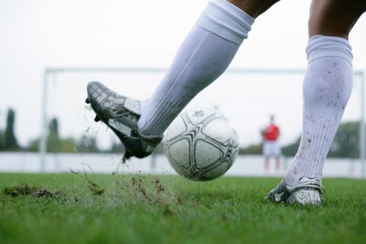 Close-up of a soccer player kicking a ball with motion and intensity on a grass field, showcasing action and sport.