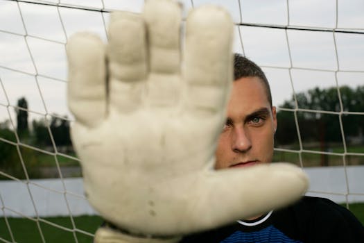Close-up of a soccer goalkeeper holding up a glove, blocking shot with intense focus.