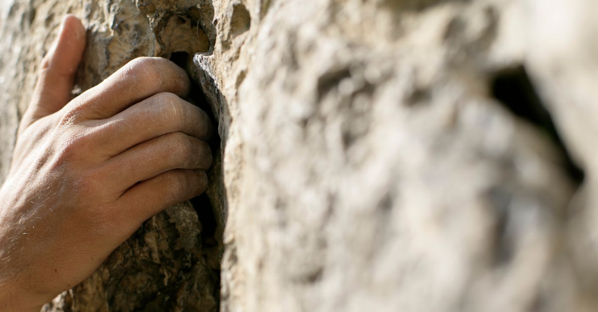 Climber's hand gripping rough rock wall through intense effort