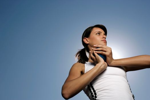 A female athlete in a white tank top concentrates intensely, ready to throw a shot put under clear blue skies.