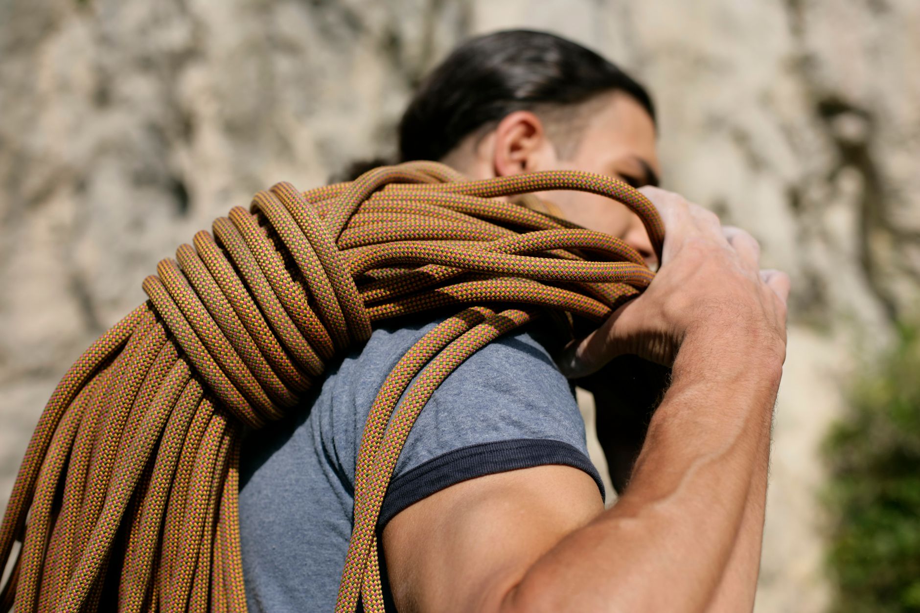 Close-up of a man carrying climbing rope, ready to ascent an outdoor rock face.