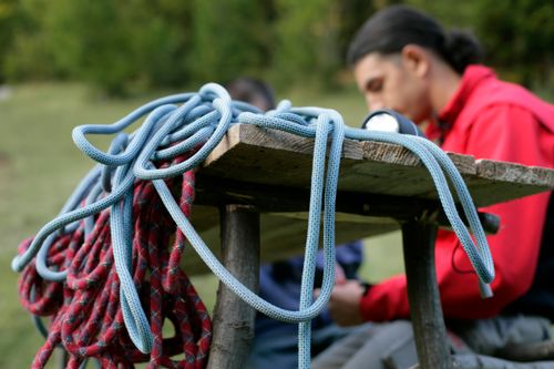 Free Close-up of climbing ropes on a wooden table with a climber in the background wearing a safety harness. Stock Photo