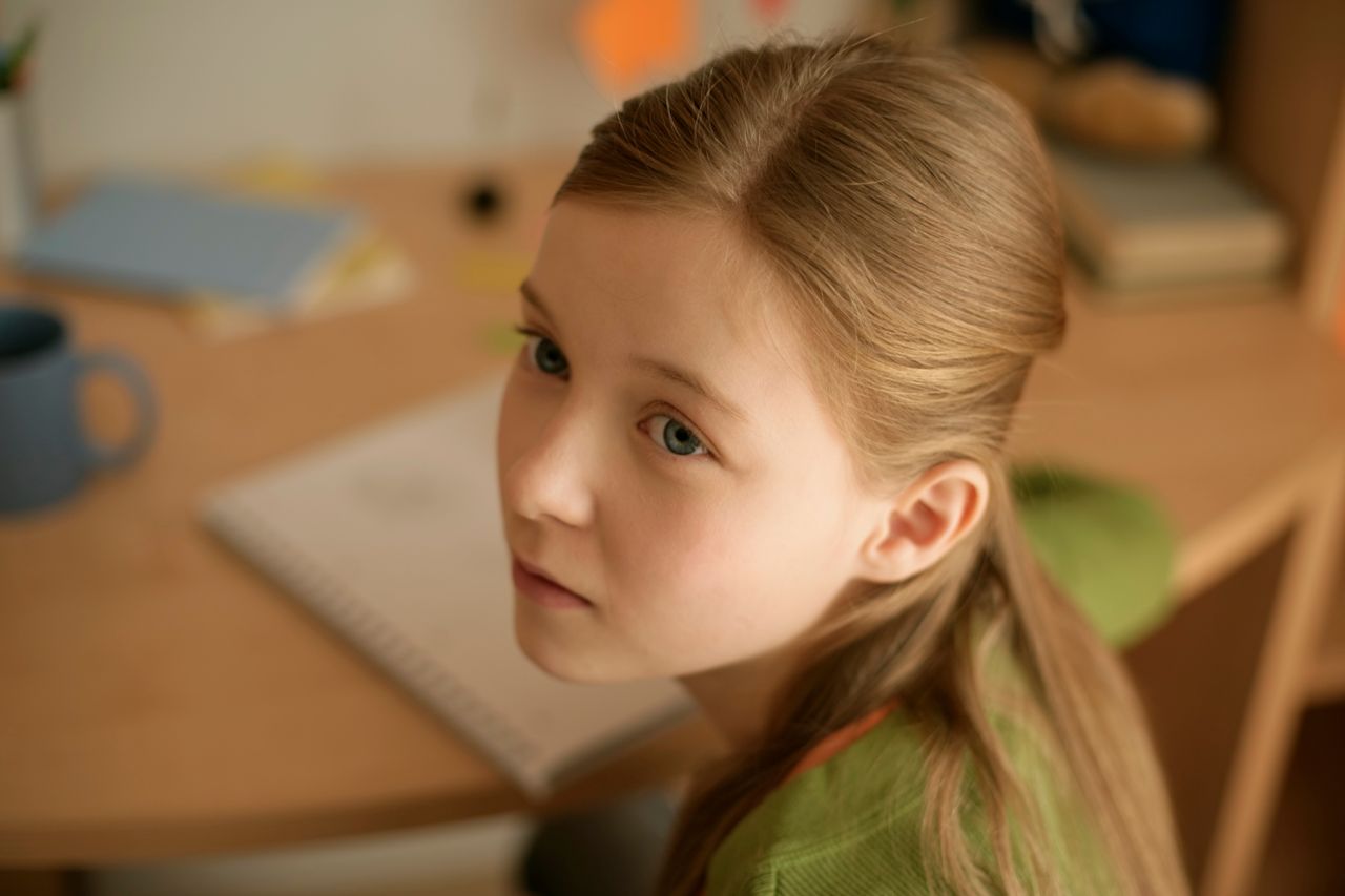 young girl sitting at a desk in a cozy room appearing thoughtful and p