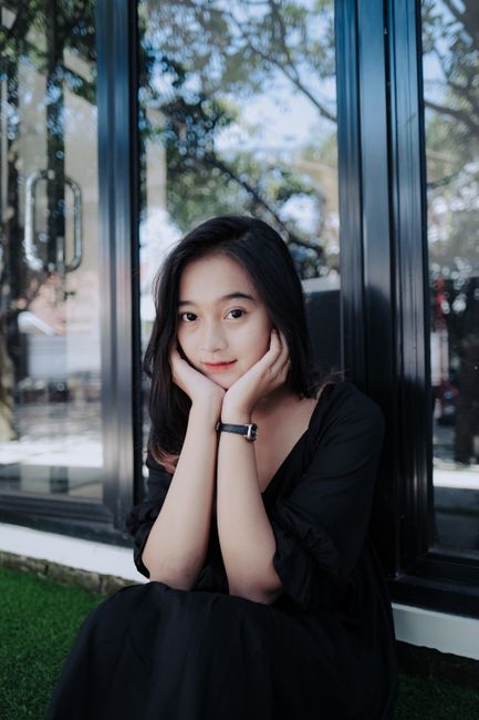 Beautiful woman sitting outdoors near glass surface, gently resting her chin on hands.