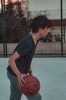 Young man with curly hair playing basketball in an outdoor court in Ankara, Türkiye.