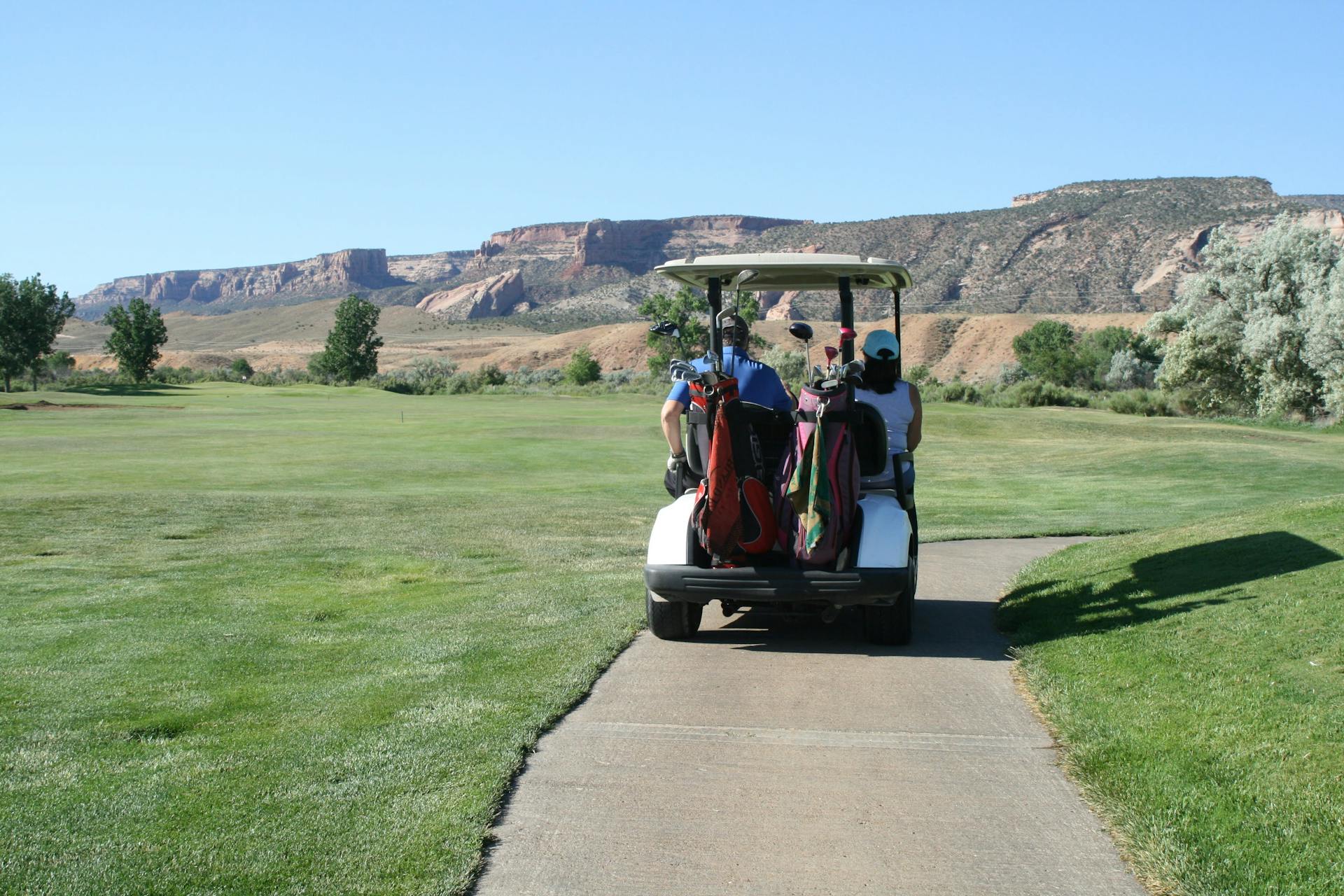 Golfers riding on a cart across a scenic golf course with mountain backdrop.