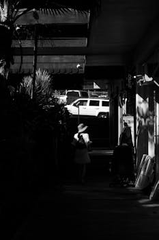 Moody black and white photo of a woman walking in Kailua-Kona, capturing urban shadows and sunlight.