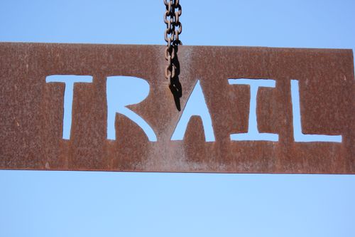 Free Close-up of a rusty trail sign hanging by a chain against a clear blue sky. Stock Photo