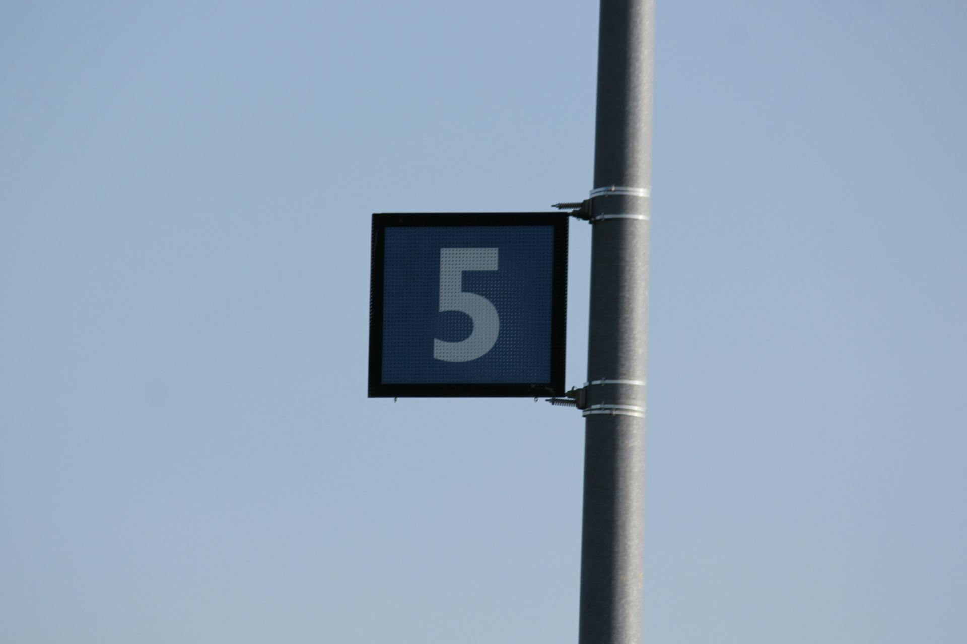 Close-up of metal pole with number 5 sign against a clear blue sky.