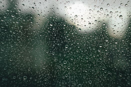 A detailed view of raindrops on glass, creating a textured pattern against a blurred backdrop.