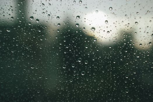 Close-up of raindrops on a glass window with blurred, overcast background outdoors.