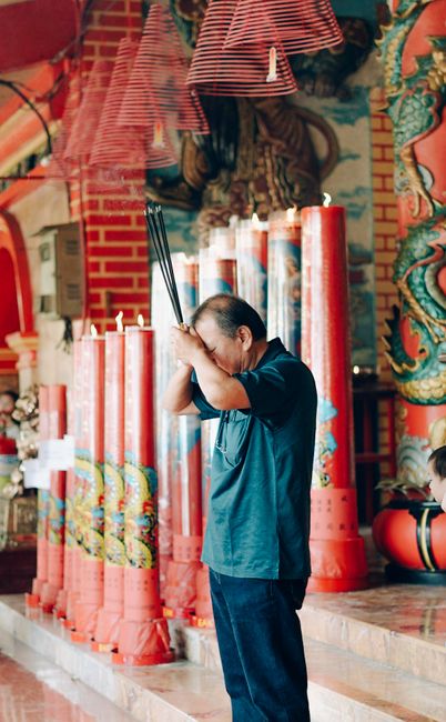 A man praying with incense sticks in a vibrant Indonesian temple depicting cultural rituals.
