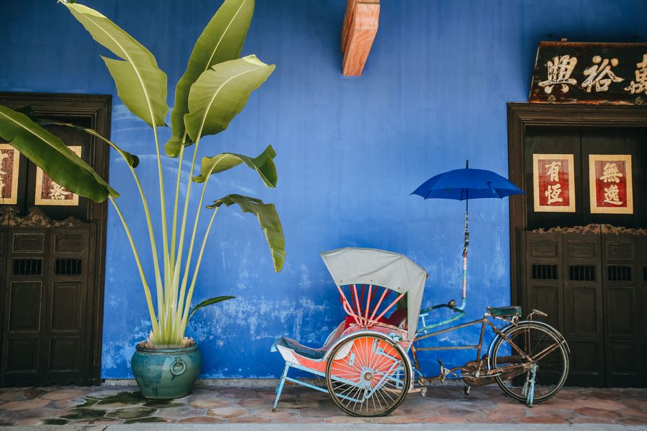 A vibrant rickshaw with umbrella against a blue wall, showcasing Malaysian heritage in George Town.
