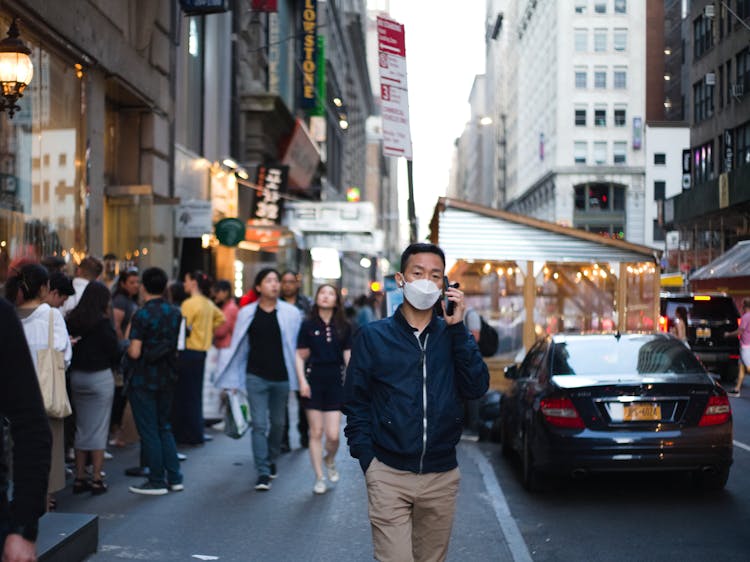 Man In A Face Mask Talking On The Phone In The City Street In Asia 