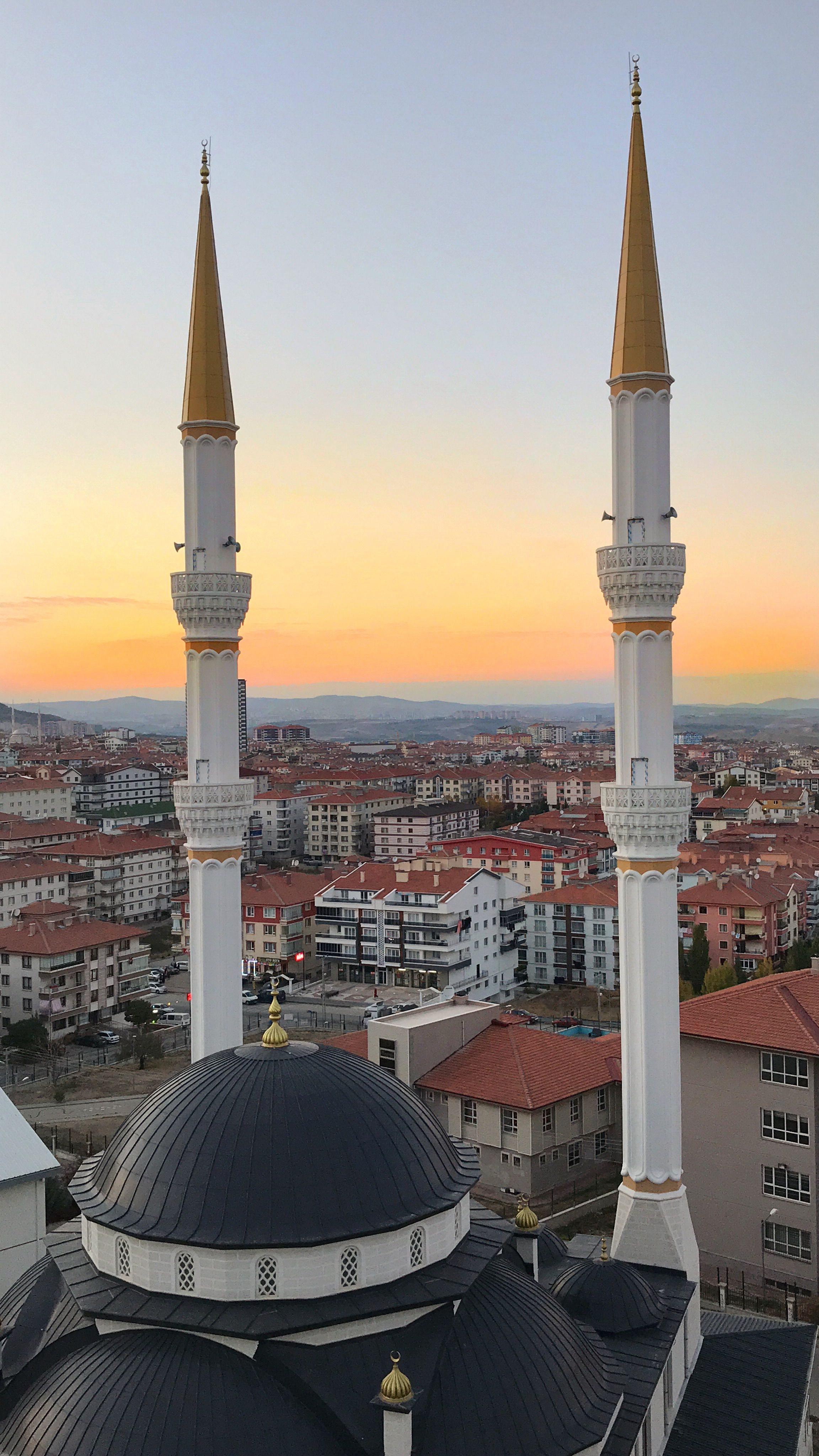 A stunning aerial shot of a mosque with minarets and city skyline at sunset.