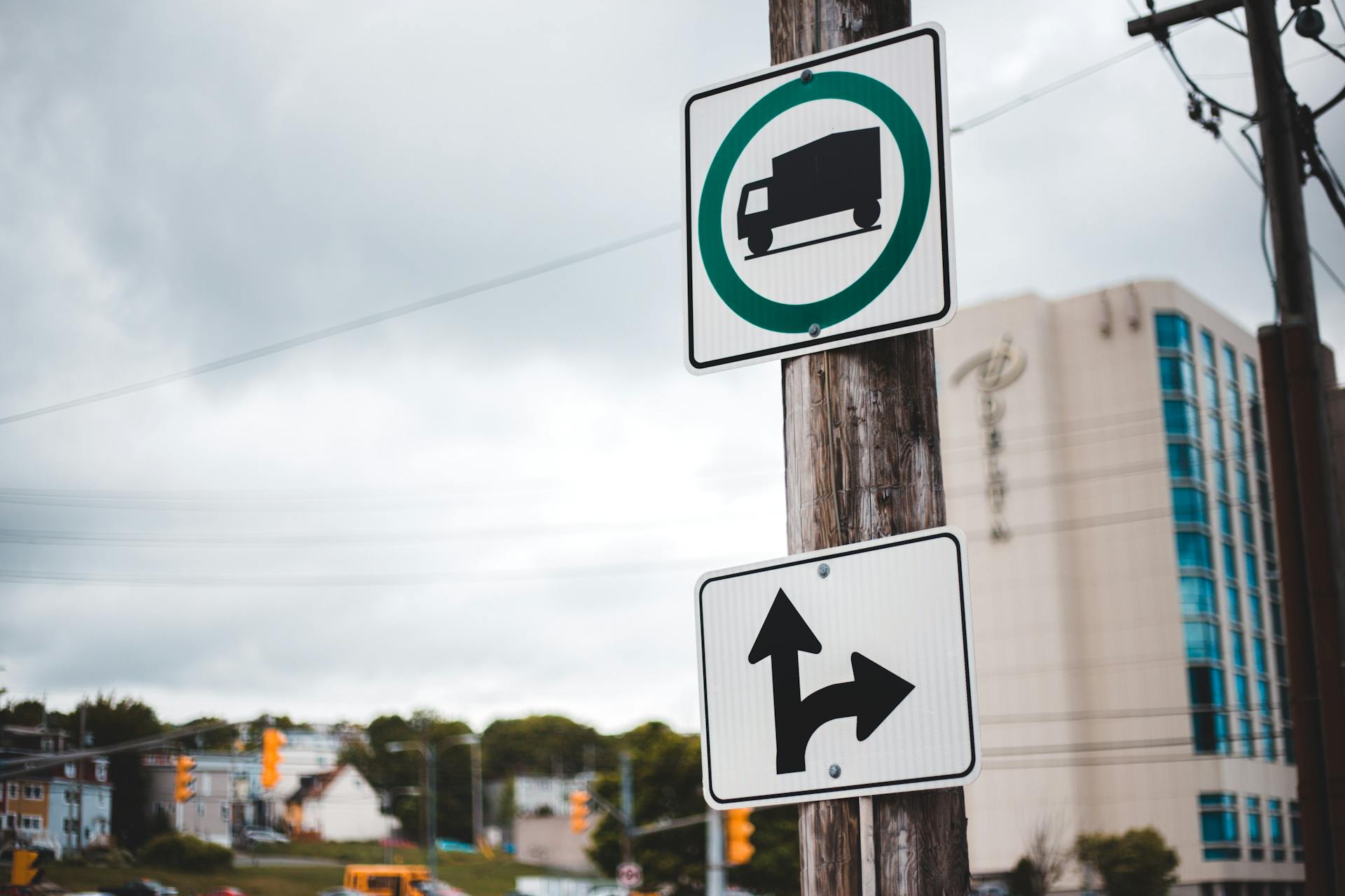 Road signs on a wooden pole against a city backdrop. Truck symbol with directional arrow.