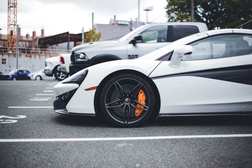 Free White McLaren sportscar parked in an urban lot showcasing its sleek design and vibrant brake calipers. Stock Photo