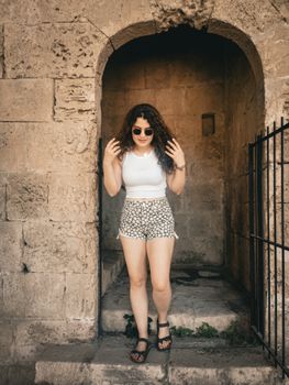 Woman with curly hair and sunglasses in Beylerbeyi, standing in a stone archway.