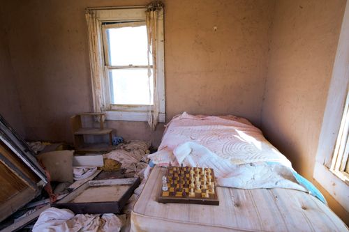 Free A desolate bedroom with unkempt bed and chessboard, conveying neglect. Stock Photo