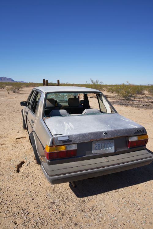 Free An old, broken car abandoned in a desert setting with a clear, blue sky. Stock Photo