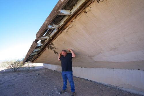 Free A man appears to support a damaged, collapsing structure in an outdoor setting. Stock Photo
