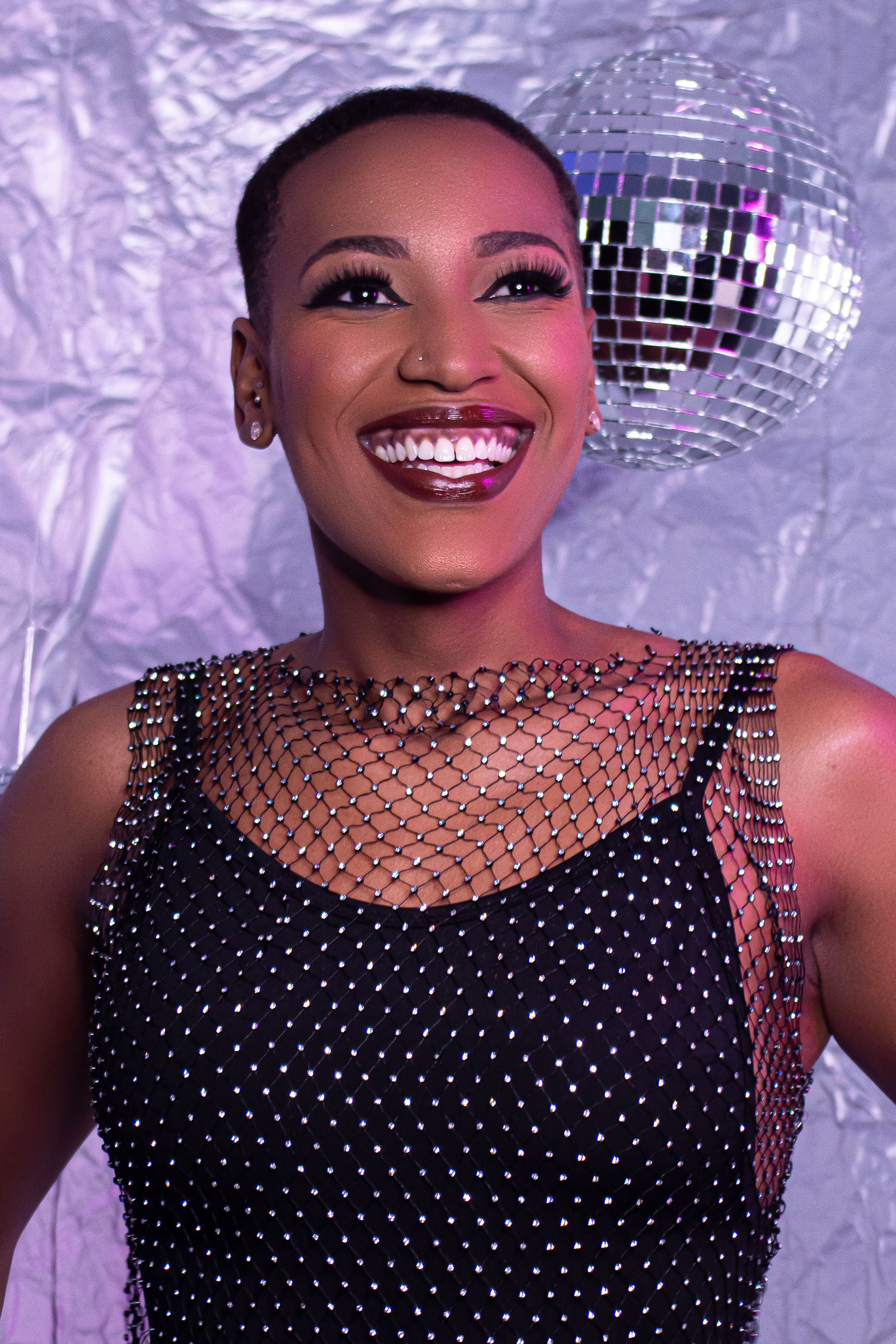 A joyful woman smiling in front of a glittering disco ball, creating a festive atmosphere.