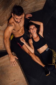 Couple taking a break from training, smiling and relaxing on gym floor.
