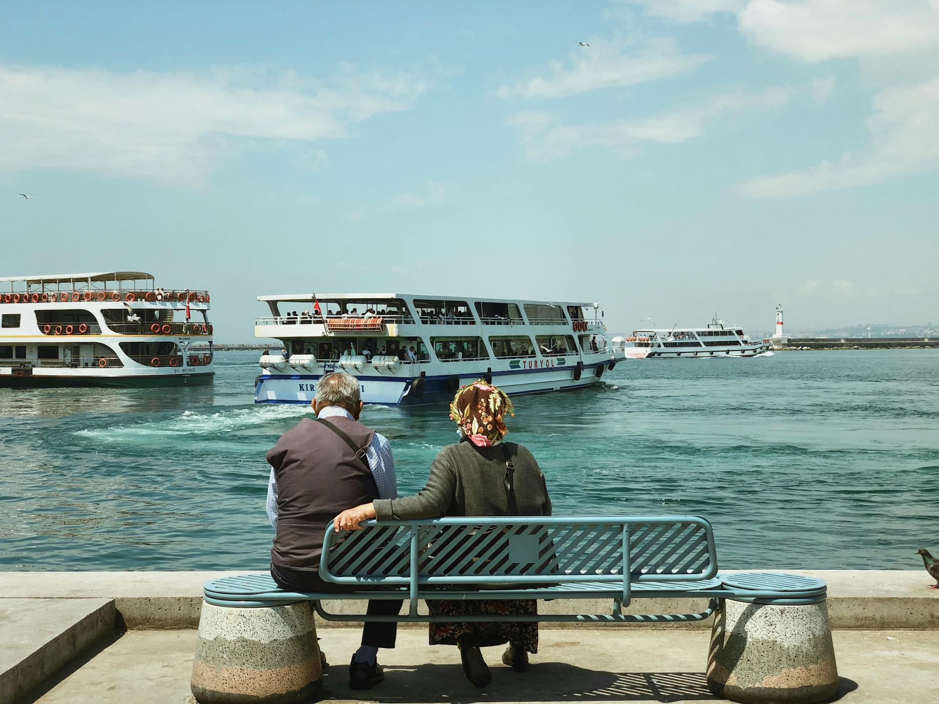 Elderly couple enjoying a calm day by the sea in İstanbul, Turkey with ferries passing by.