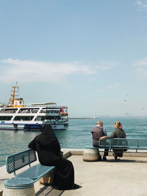 Free People sitting by the Bosphorus with a ferry passing in Istanbul, Turkey. Stock Photo