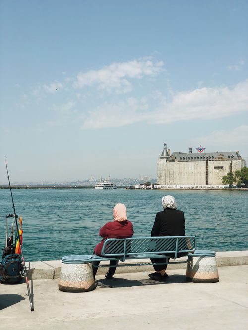 Free Two women sitting by the Bosphorus, Haydarpaşa Terminal visible, enjoying a serene day. Stock Photo
