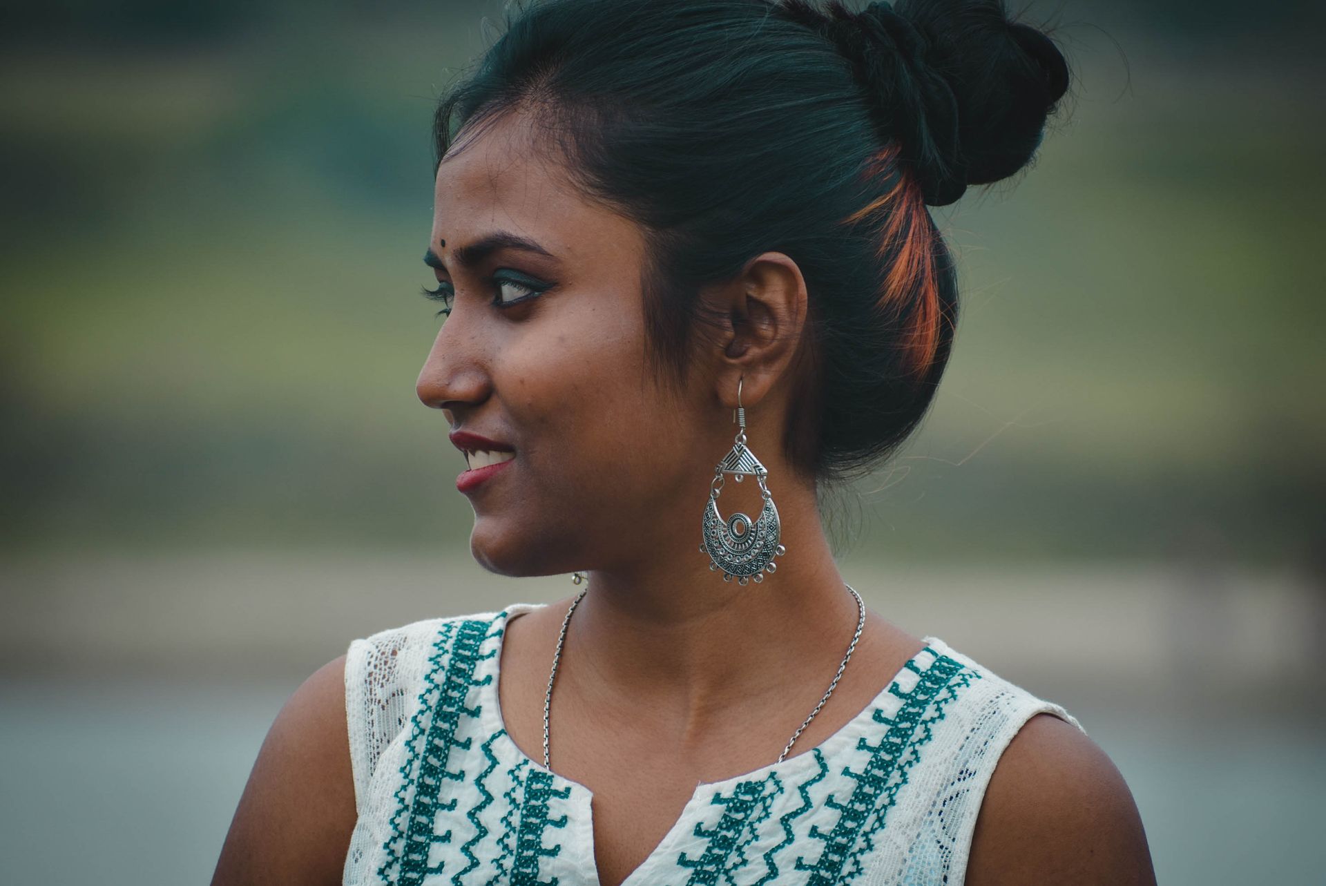 Close-up profile of a smiling woman with intricate jewelry and traditional attire outdoors.