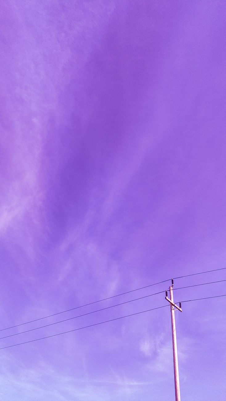 Vibrant purple sky with wispy clouds and a utility pole captured in a vertical shot.