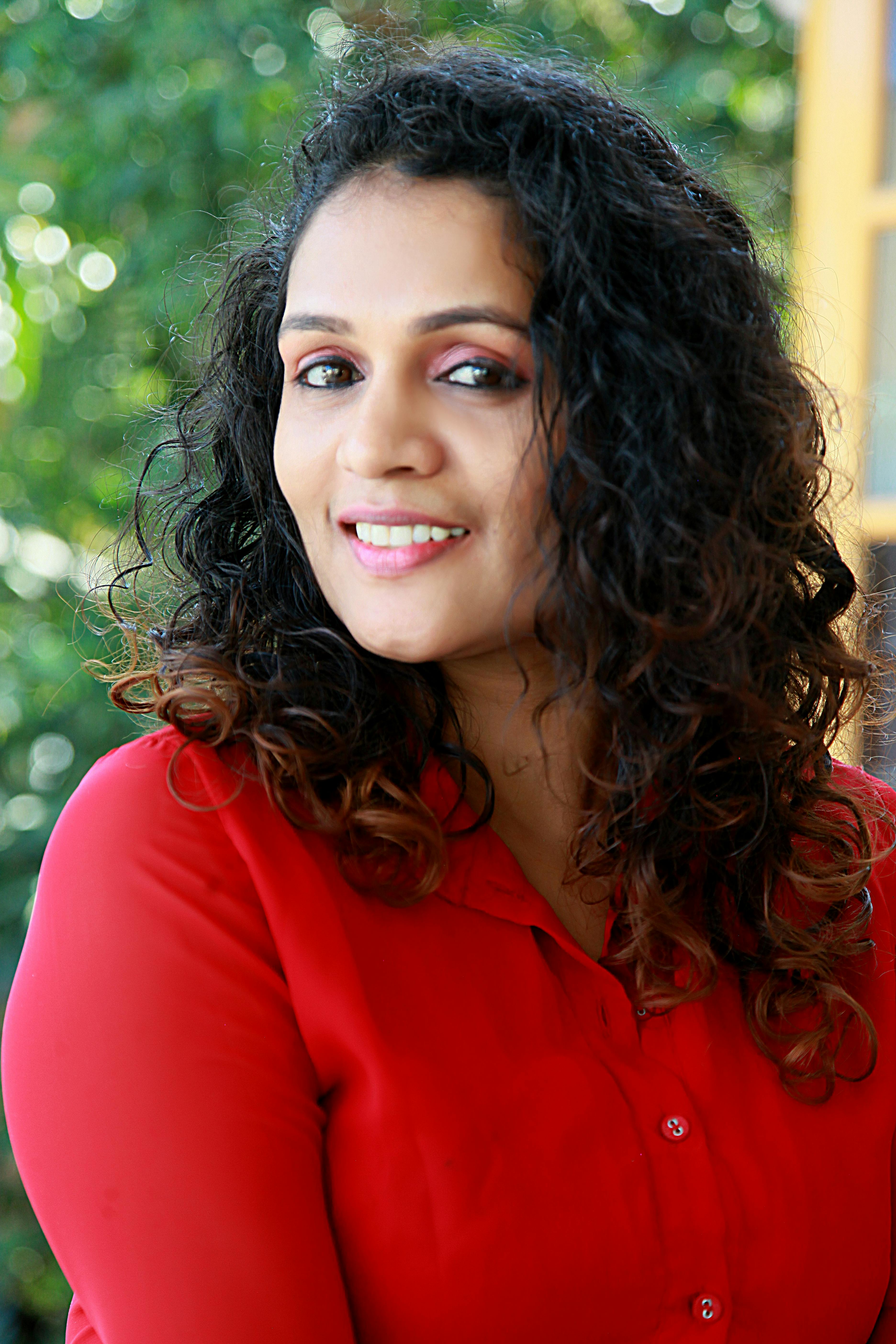 Portrait of a smiling woman with curly hair, wearing a red blouse, outdoors.