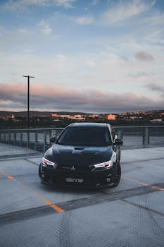 Modern black luxury car parked on a rooftop with cityscape backdrop.