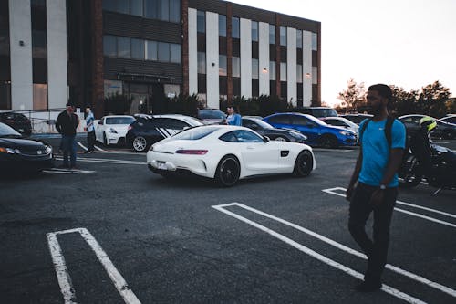 People Walking in a Parking Lot Filled With Various Sports Cars