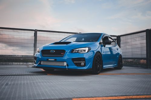 Free Vibrant blue Subaru sports car parked in an urban rooftop parking lot with a scenic sky backdrop. Stock Photo