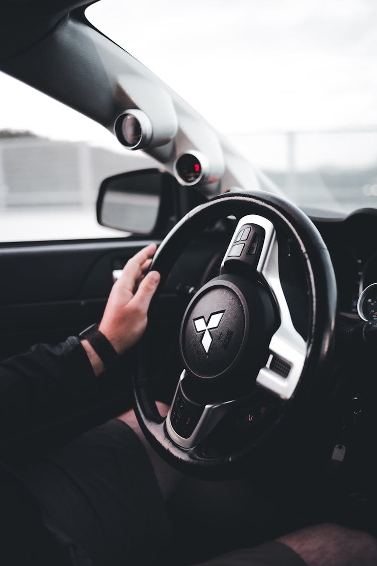 A Person Holding A Black Mitsubishi Steering Wheel