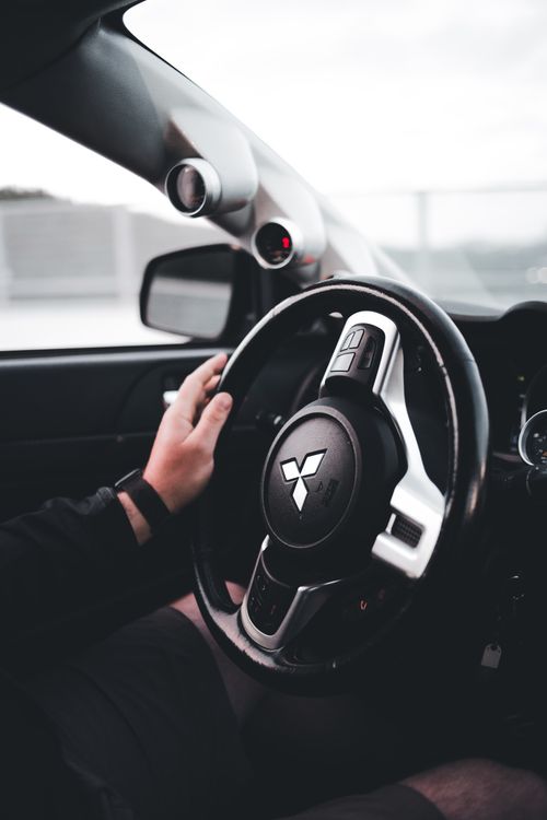Free Close-up of a person's hand on the steering wheel of a Mitsubishi car interior. Stock Photo