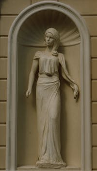 Classical female stone statue in an arched architectural niche with soft natural lighting.