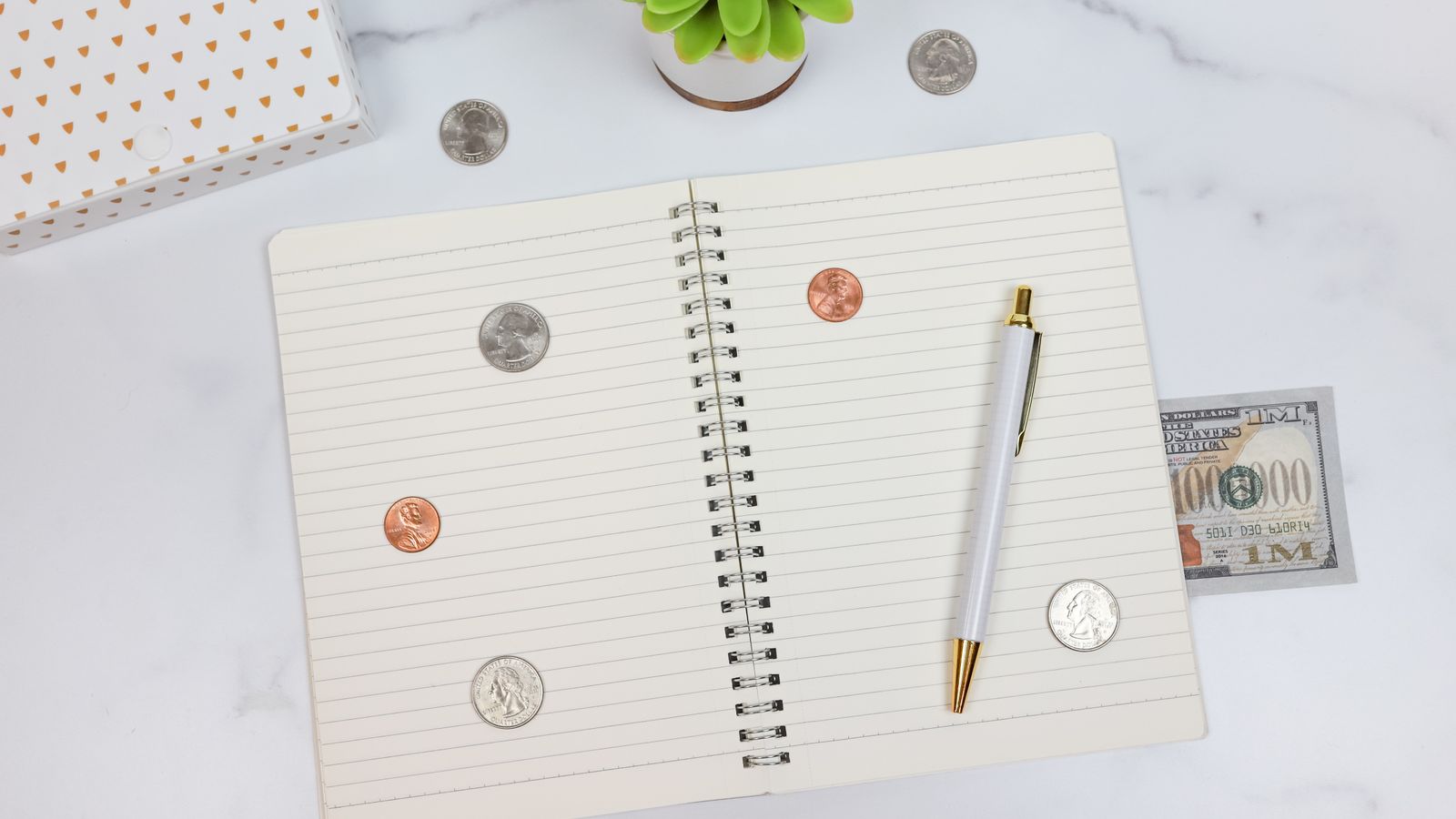 A notebook, pen and cash arranged on a marble desk