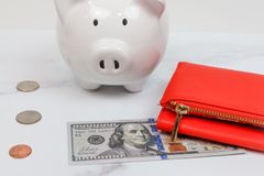 White piggy bank with coins and a red wallet on a marble desk.