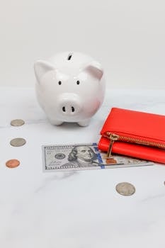 White piggy bank with coins and a red wallet on a marble desk.