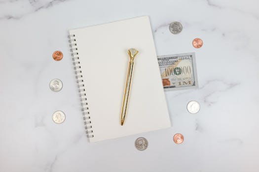 Stylish flat lay of a notebook with coins and a $100 bill on a marble surface.