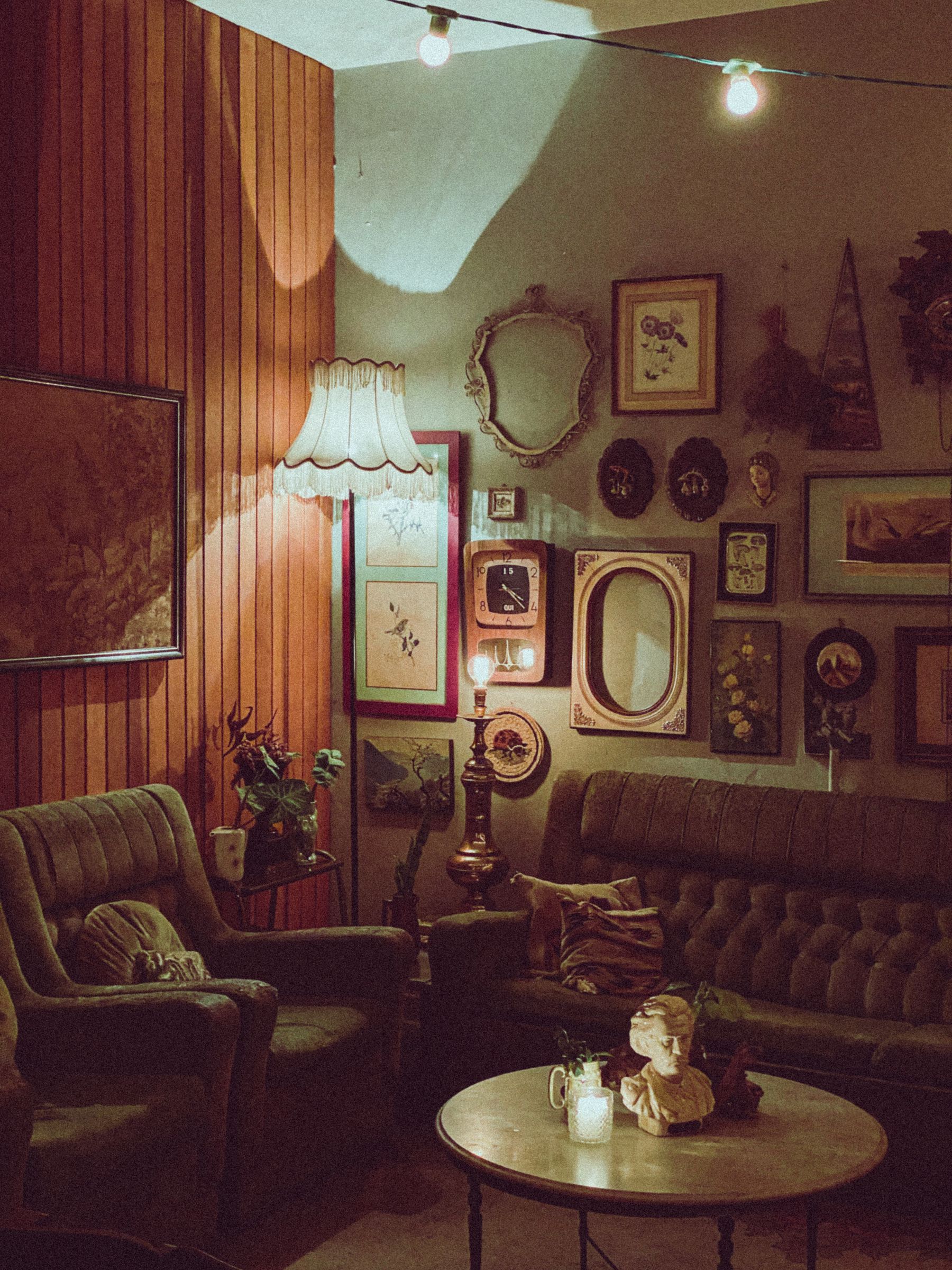 Collected living room combining brown paneling, sofa, chair, table and framed objects in distinct materials