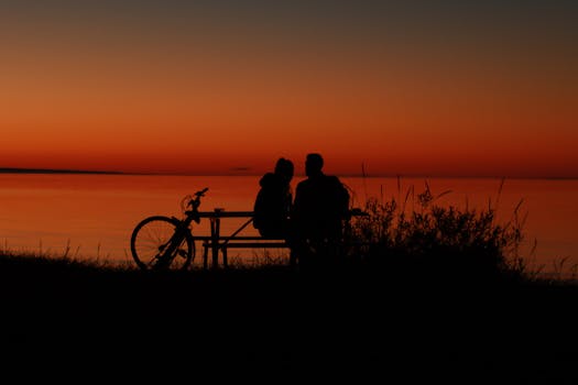 Couple sits at sunset with a bike by the serene shore in Jönköping, Sweden.