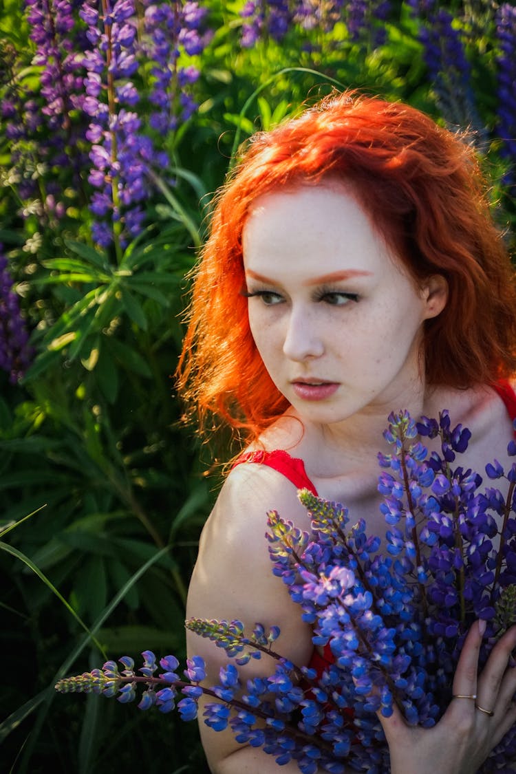 A Woman With Red Hair Holding A Bouquet Of Lupine Flowers