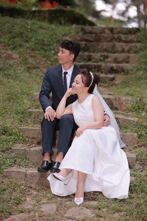 Photo of a Groom and a Bride Sitting on Concrete Stairs