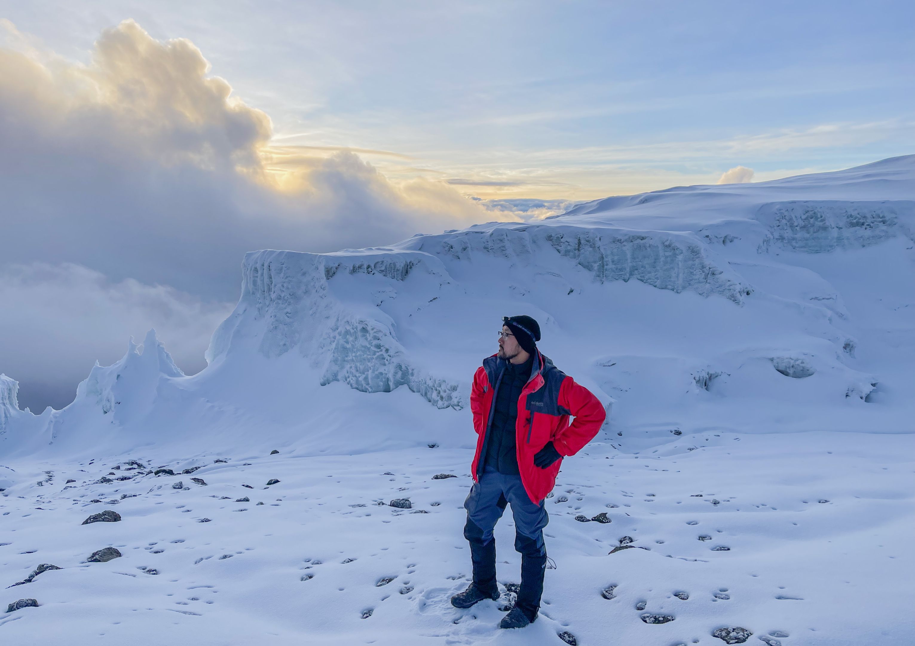 A climber at the snowy summit of Mount Kilimanjaro at sunrise, wearing a red jacket