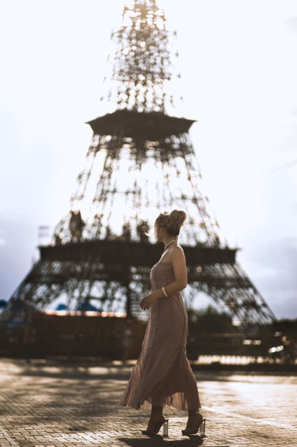 Stylish woman in elegant dress walking near the iconic Eiffel Tower in Paris.