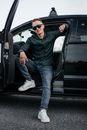 Man Sitting in a Car with Legs Out on the Road and Smiling